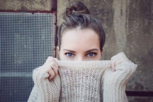 woman with blue eyes holding her sweater over her mouth and nose