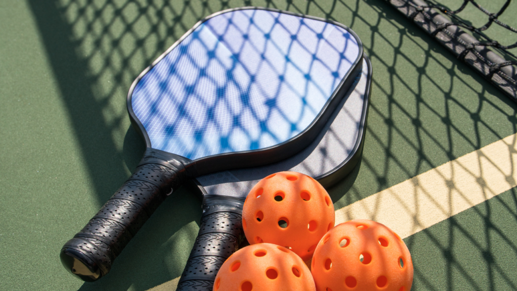 two blue pickleball paddles and three orange pickleballs sitting on a green court